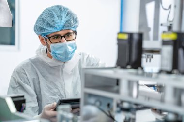 Yüz maskeli üretim hattı işçisi elektronik fabrikasında çalışıyor.