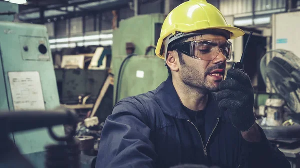 Trabajador de fábrica hablando por radio portátil mientras inspecciona piezas de maquinaria — Foto de Stock