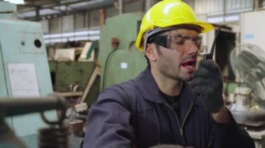 Fabrika işçisi, makine parçalarını incelerken taşınabilir radyodan konuşuyor.