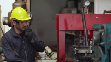 Fabrika işçisi, makine parçalarını incelerken taşınabilir radyodan konuşuyor.