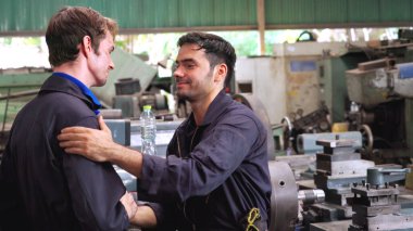 Yorgun fabrika işçileri mola verip fabrikada iş arkadaşlarıyla konuşuyorlar.