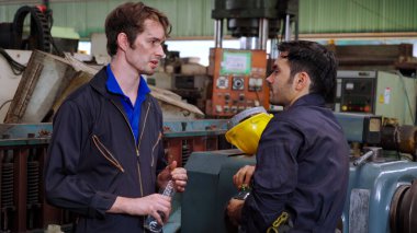 Yorgun fabrika işçileri mola verip fabrikada iş arkadaşlarıyla konuşuyorlar.