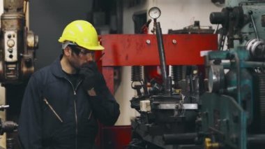 Fabrika işçisi, makine parçalarını incelerken taşınabilir radyodan konuşuyor.