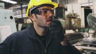 Fabrika işçisi, makine parçalarını incelerken taşınabilir radyodan konuşuyor.