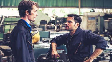 Yorgun fabrika işçileri mola verip fabrikada iş arkadaşlarıyla konuşuyorlar.