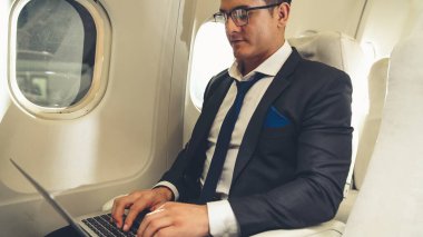 Genç işadamı uçakta dizüstü bilgisayar kullanıyor.