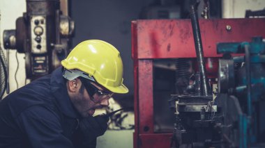 Fabrika işçisi, makine parçalarını incelerken taşınabilir radyodan konuşuyor.