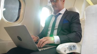 Genç işadamı uçakta dizüstü bilgisayar kullanıyor.