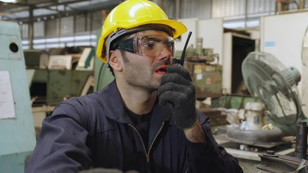 Pracownik fabryki rozmawia przez przenośne radio podczas kontroli części maszyn — Zdjęcie stockowe
