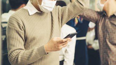 Trende cep telefonu kullanan gezgin yüz maskesi takıyor