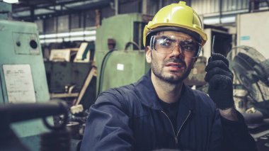 Fabrika işçisi, makine parçalarını incelerken taşınabilir radyodan konuşuyor.