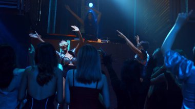 Bir grup insan disko gece kulübünde DJ 'in sahnede çaldığı müzikle dans ediyor.