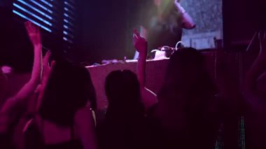 Bir grup insan disko gece kulübünde DJ 'in sahnede çaldığı müzikle dans ediyor.
