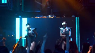 Bir grup insan disko gece kulübünde DJ 'in sahnede çaldığı müzikle dans ediyor.
