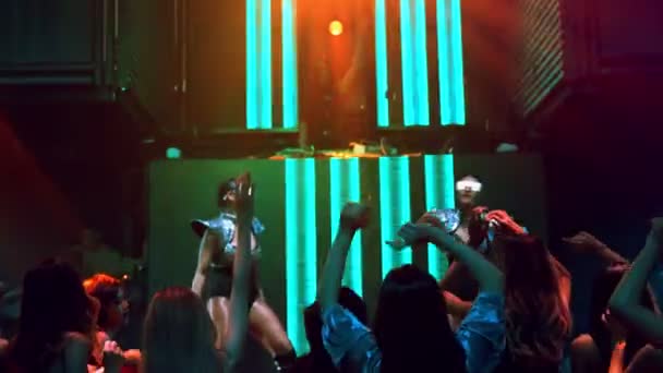 Group of people dance in disco night club to the beat of music from DJ on stage — Stock Video