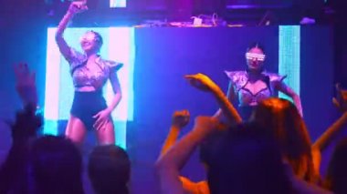 Bir grup insan disko gece kulübünde DJ 'in sahnede çaldığı müzikle dans ediyor.