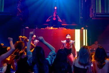 Bir grup insan disko gece kulübünde DJ 'in sahnede çaldığı müzikle dans ediyor.