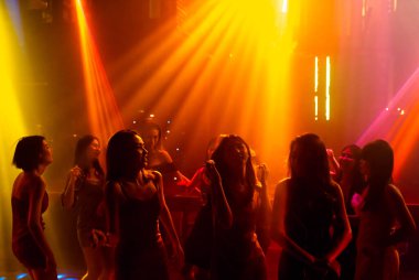 Disko gece kulübünde DJ 'in sahnede yaptığı müzikle dans eden insanların silueti.