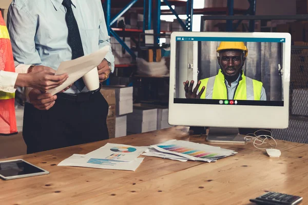 Warehouse staff talking on video call at computer screen in storage warehouse