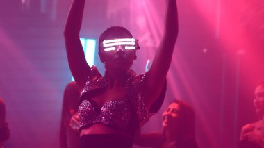 Bir grup insan disko gece kulübünde DJ 'in sahnede çaldığı müzikle dans ediyor.