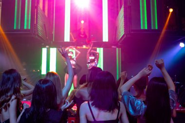 Bir grup insan disko gece kulübünde DJ 'in sahnede çaldığı müzikle dans ediyor.
