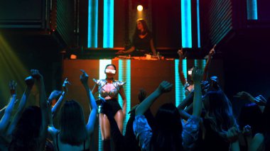 Bir grup insan disko gece kulübünde DJ 'in sahnede çaldığı müzikle dans ediyor.