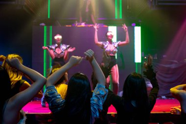 Bir grup insan disko gece kulübünde DJ 'in sahnede çaldığı müzikle dans ediyor.