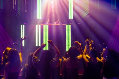 Disko gece kulübünde DJ 'in sahnede yaptığı müzikle dans eden insanların silueti.