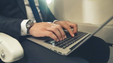 Genç işadamı uçakta dizüstü bilgisayar kullanıyor.