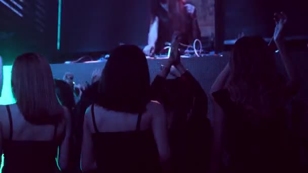 Groep mensen dansen in disco nachtclub op de beat van muziek van DJ op het podium — Stockvideo