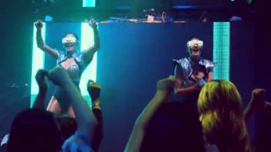 Bir grup insan disko gece kulübünde DJ 'in sahnede çaldığı müzikle dans ediyor.