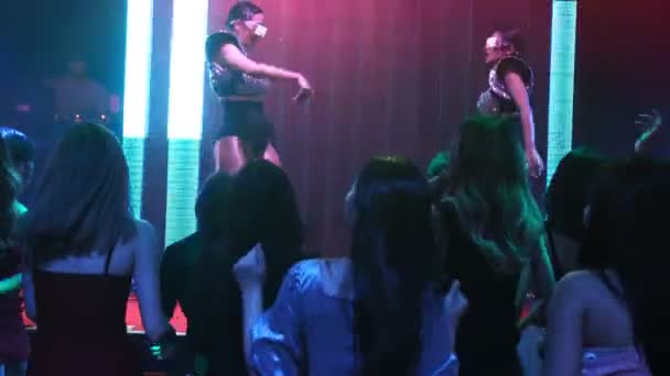 Group of people dance in disco night club to the beat of music from DJ on stage — Stock Video