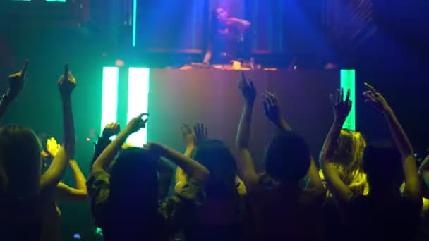 Group of people dance in disco night club to the beat of music from DJ on stage — Stock Video