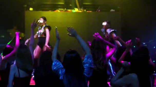 Group of people dance in disco night club to the beat of music from DJ on stage — Stock Video