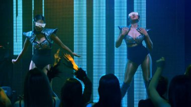 Bir grup insan disko gece kulübünde DJ 'in sahnede çaldığı müzikle dans ediyor.