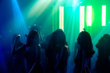 Disko gece kulübünde DJ 'in sahnede yaptığı müzikle dans eden insanların silueti.