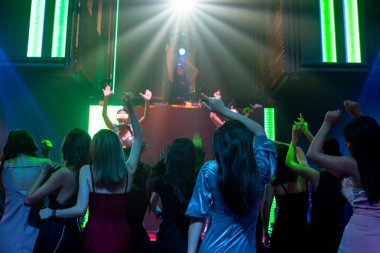 Bir grup insan disko gece kulübünde DJ 'in sahnede çaldığı müzikle dans ediyor.