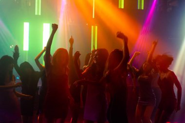Disko gece kulübünde DJ 'in sahnede yaptığı müzikle dans eden insanların silueti.