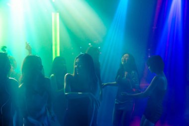 Disko gece kulübünde DJ 'in sahnede yaptığı müzikle dans eden insanların silueti.