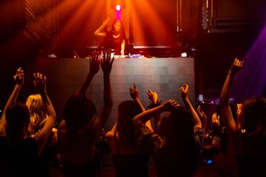 Disko gece kulübünde DJ 'in sahnede yaptığı müzikle dans eden insanların silueti.