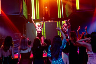Bir grup insan disko gece kulübünde DJ 'in sahnede çaldığı müzikle dans ediyor.