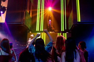 Bir grup insan disko gece kulübünde DJ 'in sahnede çaldığı müzikle dans ediyor.