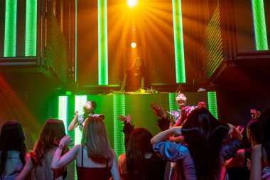 Bir grup insan disko gece kulübünde DJ 'in sahnede çaldığı müzikle dans ediyor.
