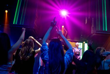 Bir grup insan disko gece kulübünde DJ 'in sahnede çaldığı müzikle dans ediyor.