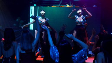 Bir grup insan disko gece kulübünde DJ 'in sahnede çaldığı müzikle dans ediyor.