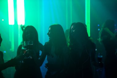 Disko gece kulübünde DJ 'in sahnede yaptığı müzikle dans eden insanların silueti.