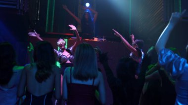 Bir grup insan disko gece kulübünde DJ 'in sahnede çaldığı müzikle dans ediyor.