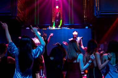 Bir grup insan disko gece kulübünde DJ 'in sahnede çaldığı müzikle dans ediyor.