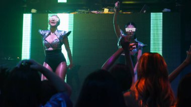 Bir grup insan disko gece kulübünde DJ 'in sahnede çaldığı müzikle dans ediyor.