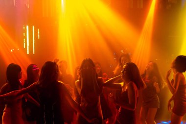 Disko gece kulübünde DJ 'in sahnede yaptığı müzikle dans eden insanların silueti.